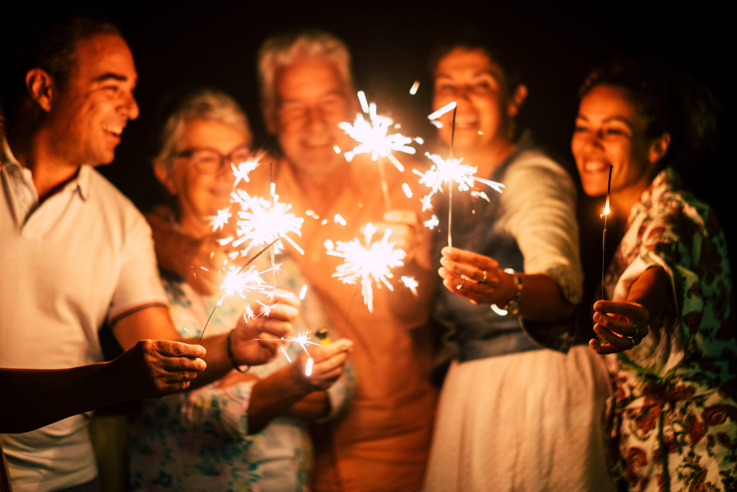 group of people have fun celebrating together new year eve or birthday with sparkles light and fireworks in friendship outdoor at evening time – family and friends different ages celebrate friendly